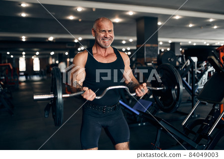 Muscular older man working out in gym doing exercises with barbell at biceps. Bodybuilding concept Muscular older man working out in gym doing exercises with barbell at biceps. Bodybuilding concept 84049003