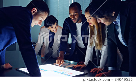 Slow motion multinational group meeting while looking at the screen at the office at night Slow motion multinational group meeting while looking at the screen at the office at night 84049535