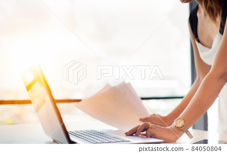 Business women working in office feeling refreshed in the morning, smiling face receiving golden light. Wear casual dresses ready for work and a laptop placed on the working desk. 84050804