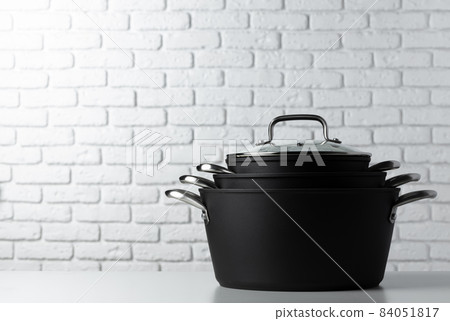 Black kitchenware on table against white brick wall 84051817