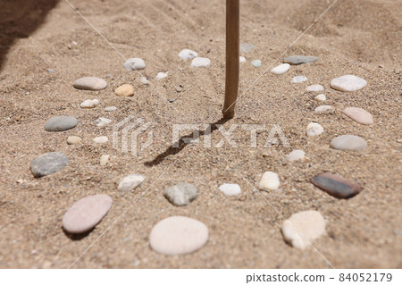 Wooden stick and pebbles on sand showing time by shadow 84052179