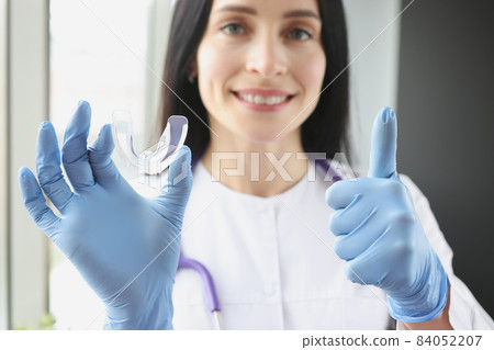 Stomatologist holding mouthguard for teeth and showing thumb up sign Stomatologist holding mouthguard for teeth and showing thumb up sign 84052207