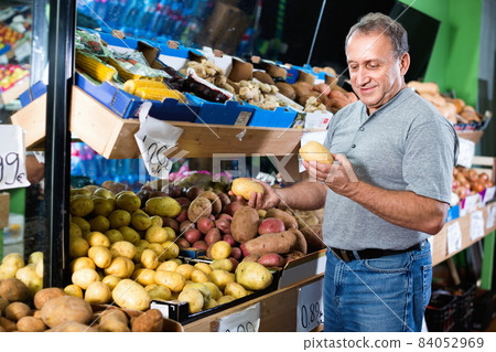 Smiling male is choosing potato in the supermarket. Smiling male is choosing potato in the supermarket. 84052969