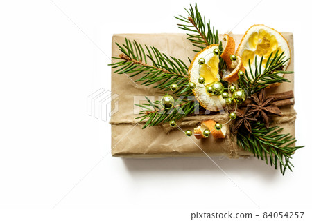 Top view on christmas gift box decorated with fresh fir twigs, dried orange slices and peels and anise stars on white background Top view on christmas gift box decorated with fresh fir twigs, dried orange slices and peels and anise stars on white background 84054257