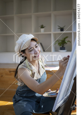 Asian woman painter sitting in front of the canvas and painting with water color at workshop. Asian woman painter sitting in front of the canvas and painting with water color at workshop. 84054277