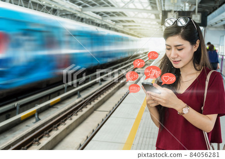 Asian woman passenger using mobile phone to check social network application with number of Like, Love, comment, people and fovorite icon in the Skytrain rails or subway in city, Social media concept, 84056281