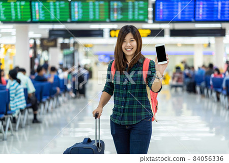 Asian traveler with luggage showing the smart mobile phone for check-in over the flight board at the flight information screen in modern an airport, travel and transportation with technology concept. 84056336