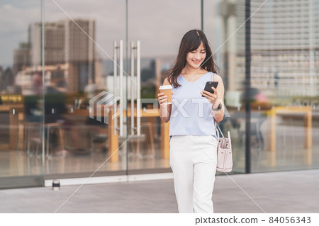 Asian woman walking in the city and using the mobile phone and holding a paper cup of coffee. department store shopping center, lifestyle and leisure, online shopping and cashless payment concept Asian woman walking in the city and using the mobile phone and holding a paper cup of coffee. department store shopping center, lifestyle and leisure, online shopping and cashless payment concept 84056343