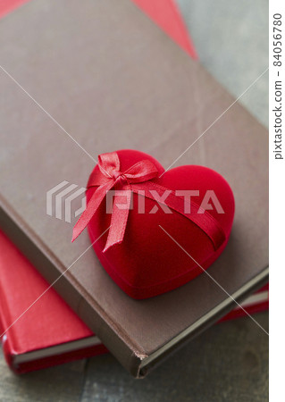 A red heart-shaped gift box placed on an antique book A red heart-shaped gift box placed on an antique book 84056780