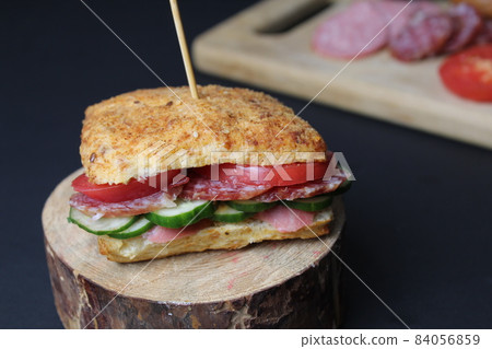 sandwich sandwich with ham sausage and vegetables cucumber tomato on a wooden stand on a black background. The serving in the restaurant is original. copyspace 84056859