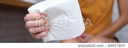 Woman sits on toilet and holds toilet paper in hands Woman sits on toilet and holds toilet paper in hands 84057854
