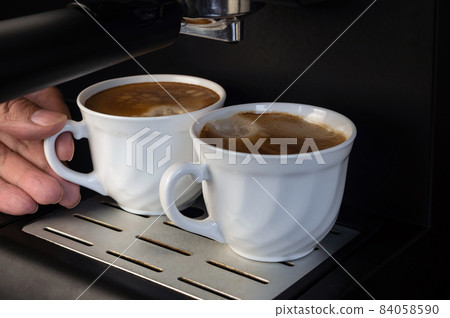 Coffee machine Two white cups of espresso coffee stand on a wire rack Coffee machine Two white cups of espresso coffee stand on a wire rack 84058590