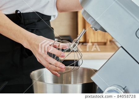 Woman put in whisk nozzle in electric mixer 84058728