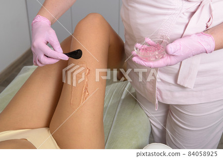 woman beautician applies contact gel on the leg of a woman for laser hair removal in medical clinic. Close up 84058925