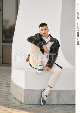 Relaxed man in plaid jacket, white turtleneck and trousers sits on the street 84059927