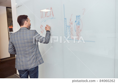 Caucasian adult man in office is writing on the glass desk 84060262