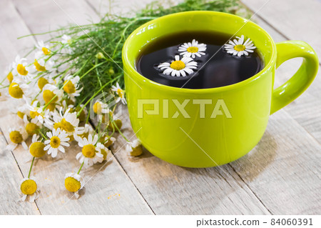 Black tea in a green cup on a wooden background and chamomile 84060391