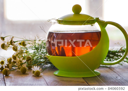 Black tea in a green cup on a wooden background and chamomile 84060392