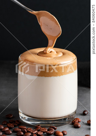 Dalgona coffee on a black background. The process of making a trendy drink. Fluffy sweet foam in a glass with ice milk. Vertical photo Dalgona coffee on a black background. The process of making a trendy drink. Fluffy sweet foam in a glass with ice milk. Vertical photo 84060475