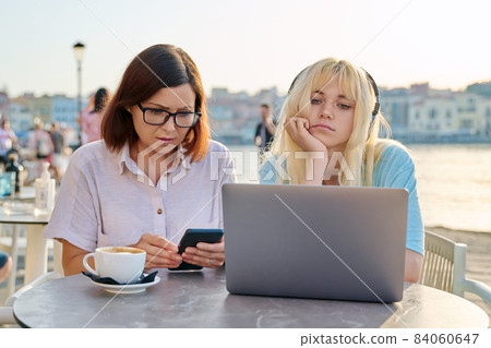 Serious mother and teenage daughter together in outdoor cafe looking at laptop 84060647