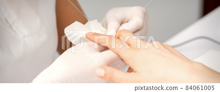 Manicure master wiping the moisturizer from the end of female fingers in beauty salon. Manicure master wiping the moisturizer from the end of female fingers in beauty salon. 84061005