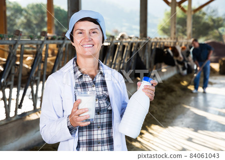 farmer in white robe posing background of cows in stall with milk 84061043
