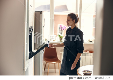 Professional confident woman is preparing custard cakes at light modern kitchen at home Professional confident woman is preparing custard cakes at light modern kitchen at home 84061096