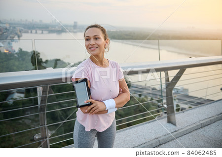 Beautiful sportswoman in sportswear smiles toothy smile standing with crossed arms on the city bridge, ready for morning jog at sunrise. Outdoor workout, healthy active lifestyle, weight loss concept Beautiful sportswoman in sportswear smiles toothy smile standing with crossed arms on the city bridge, ready for morning jog at sunrise. Outdoor workout, healthy active lifestyle, weight loss concept 84062485