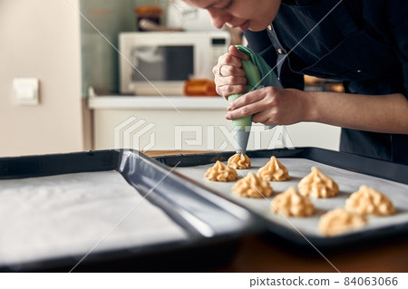 beautiful caucasian lady cook is making eclairs with help of pastry casing at home beautiful caucasian lady cook is making eclairs with help of pastry casing at home 84063066