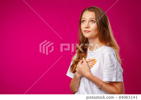 Young casual woman holding hands on her chest and looking up hopefully 84063141