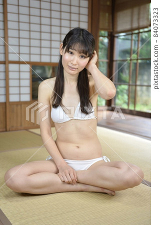 一個穿著白色比基尼泳裝的年輕女子在一座民居中的日式房間放鬆 84073323