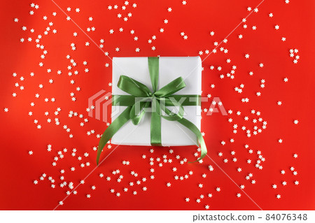 Gift box wrapped in white paper with a mint blue bow on festive crimson background with many snowflakes. Copyspace for your text. Flat lay style. Christmas, New Year or birthday celebration concept Gift box wrapped in white paper with a mint blue bow on festive crimson background with many snowflakes. Copyspace for your text. Flat lay style. Christmas, New Year or birthday celebration concept 84076348