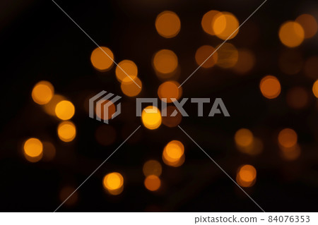 Defocused bokeh lights on black background, an abstract naturally blurred backdrop for Christmas eve or birthday party. Festive light texture. Yellow and red garland in blur. Overlay effect for design 84076353