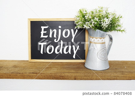 Blackboard with the text ENJOY TODAY decorate with artificial plant in watering plant on wooden shelves Blackboard with the text ENJOY TODAY decorate with artificial plant in watering plant on wooden shelves 84078408