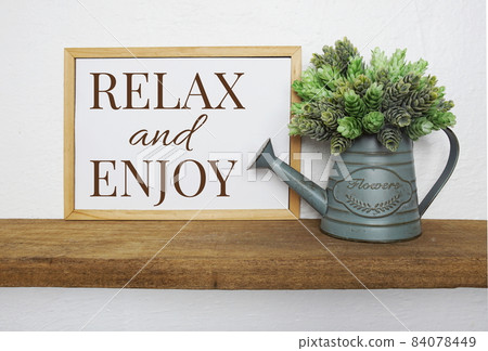 Blackboard with the text RELAX and ENJOY decorate with artificial plant in watering plant on wooden shelves Blackboard with the text RELAX and ENJOY decorate with artificial plant in watering plant on wooden shelves 84078449