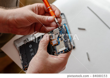 A man is repairing a Smartphone. Hands hold a screwdriver and disconnect the sim card loop. 84080153