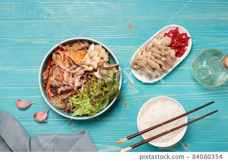 Korean cuisine or Asian . Crystal noodles with beef, vegetables and oyster mushrooms. Close-up, on a blue wooden background, with ingredients for cooking Korean cuisine or Asian . Crystal noodles with beef, vegetables and oyster mushrooms. Close-up, on a blue wooden background, with ingredients for cooking 84080354
