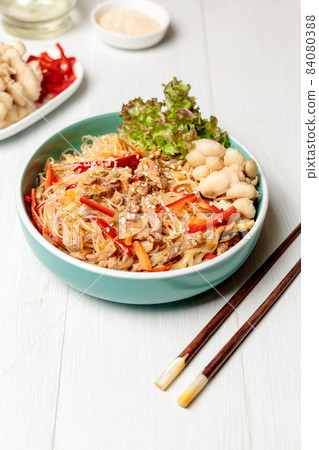Asian cuisine. Funchosa with vegetables, mushrooms and meat. Close-up. On a light wooden table with chopsticks 84080388