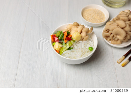 Bowl with funchosa, vegetables and oyster mushrooms. On a light wooden background, horizontal with space 84080389