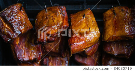 Close up of smoked meat and belly or beech meat with dark crust in the smokehouse or smoker, food concept. Close up of smoked meat and belly or beech meat with dark crust in the smokehouse or smoker, food concept. 84080719
