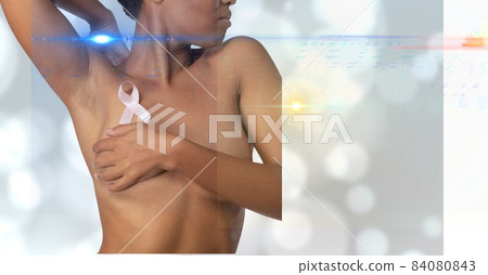 Mid section of woman wearing a pink ribbon on her chest against spots of lights on grey background 84080843