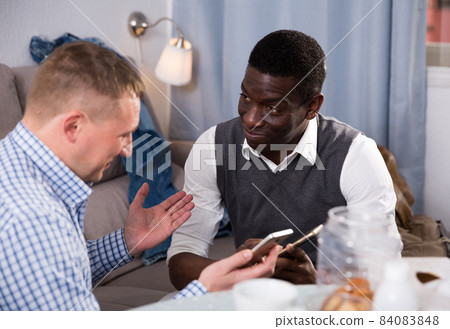 Smiling African man with phone discussing with friend at home 84083848