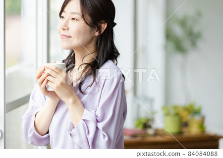 一個女人站在杯子的窗戶旁邊 84084088