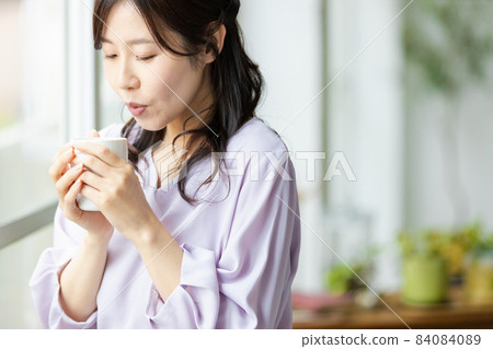 一個女人站在杯子的窗戶旁邊 84084089