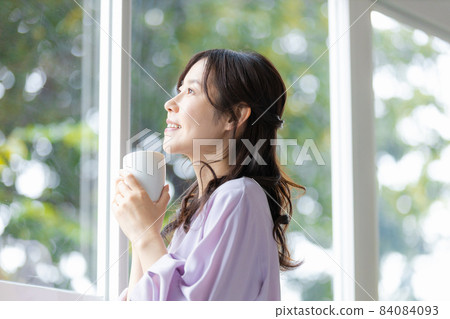 一個女人站在杯子的窗戶旁邊 一個女人站在杯子的窗戶旁邊 84084093