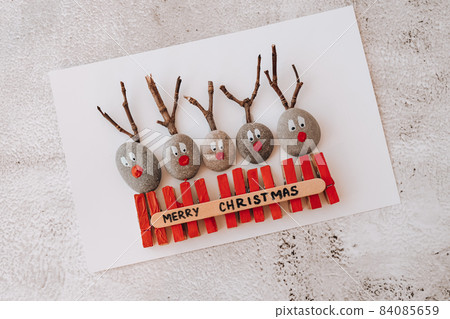 Diy Merry Christmas deer on greeting card postcard made of pebbles, sea stones, clothespins and branches on white background. Natural Eco style diy. Gift idea. Step by step. Top view. 84085659