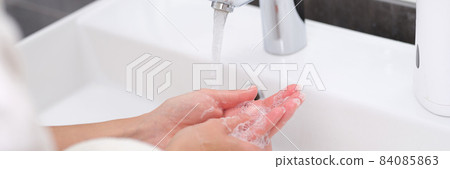 Woman washing her hands under water from tap in bathroom closeup 84085863