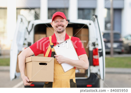 Happy postman with cardboard package and delivery receipt paper on street 84085950
