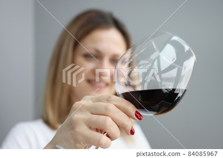 Young pretty woman holding glass of exquisite red wine and slants liquid inside Young pretty woman holding glass of exquisite red wine and slants liquid inside 84085967
