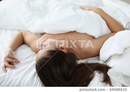 Relaxed brunette woman sleeping topless on white bedding at home 84086010